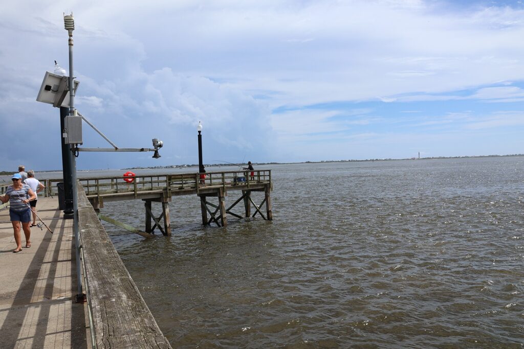 Anglers on the fishing pier at Southport Waterfront Park, looking across the Cape Fear River toward Oak Island and the Oak Island Lighthouse