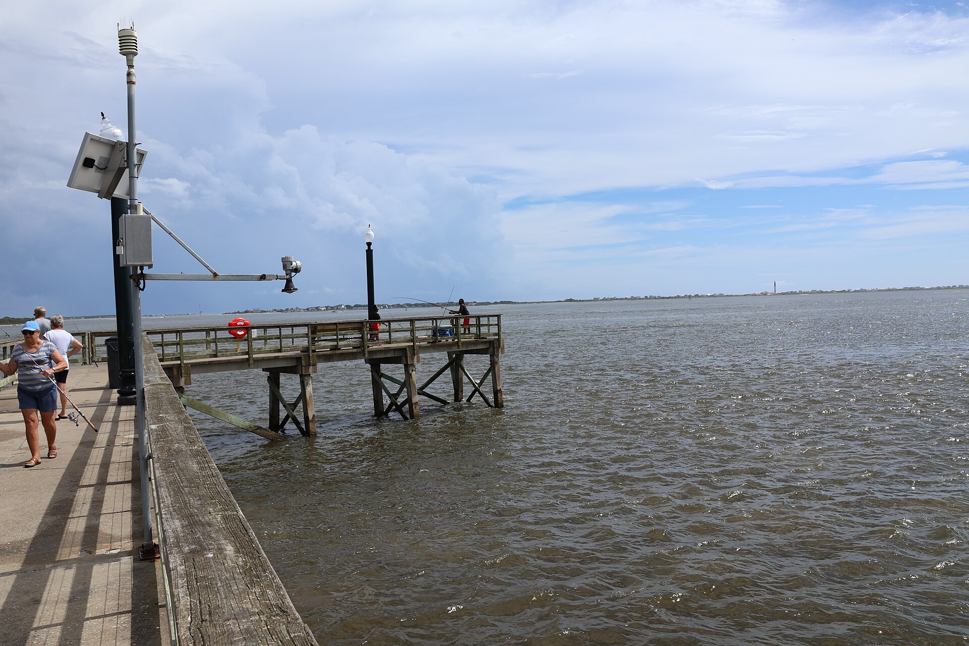 Anglers on the fishing pier at Southport Waterfront Park, looking across the Cape Fear River toward Oak Island and the Oak Island Lighthouse