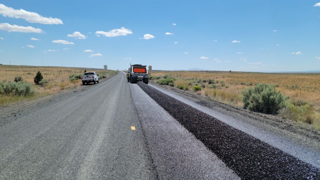 Construction equipment resurfacing a rural highway under a clear blue sky
