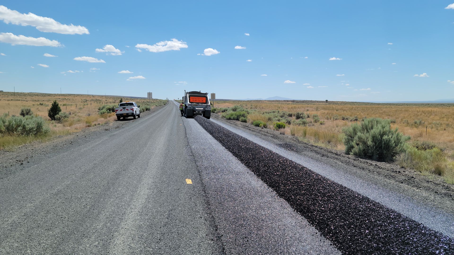 Construction equipment resurfacing a rural highway under a clear blue sky