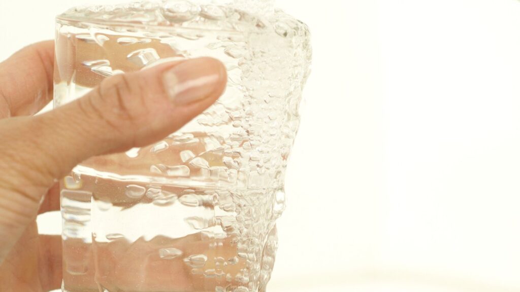 A hand holding a clear glass filling with tap water at a kitchen sink