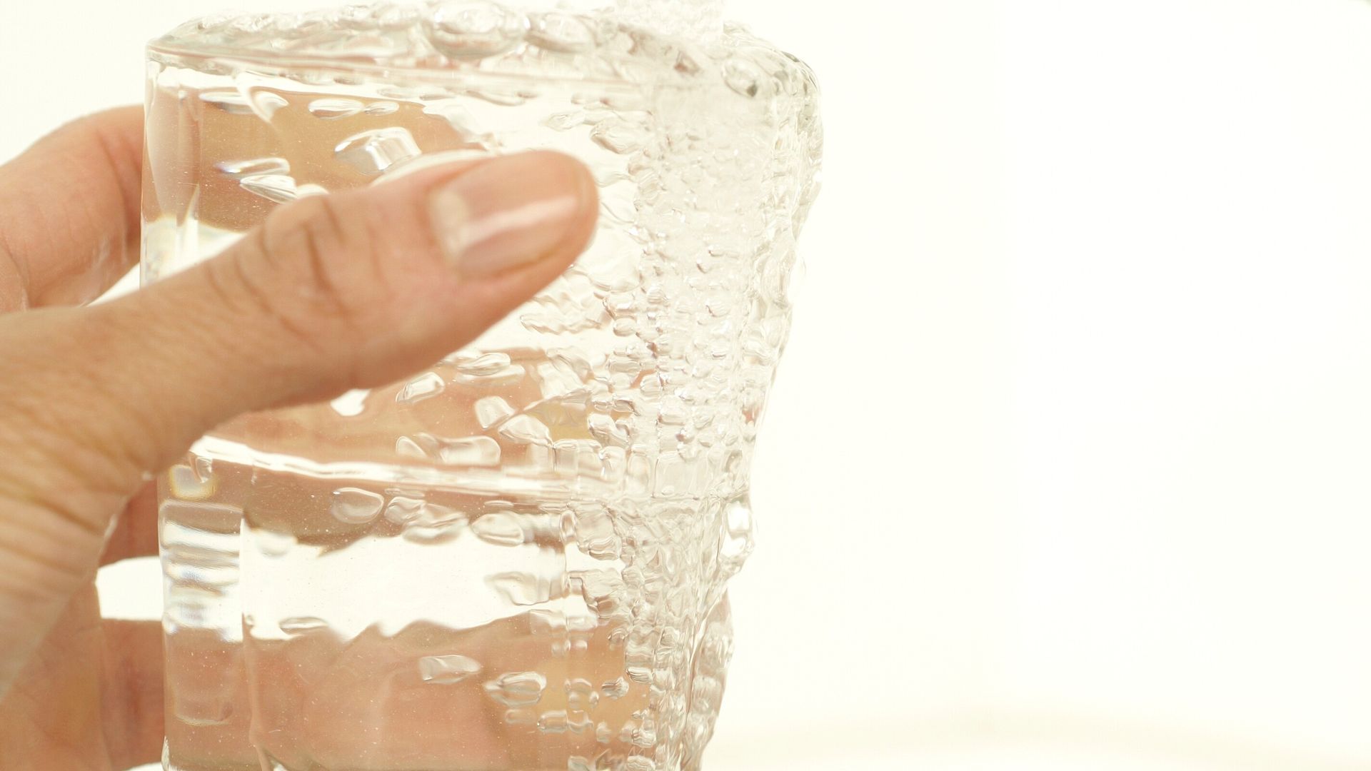 A hand holding a clear glass filling with tap water at a kitchen sink