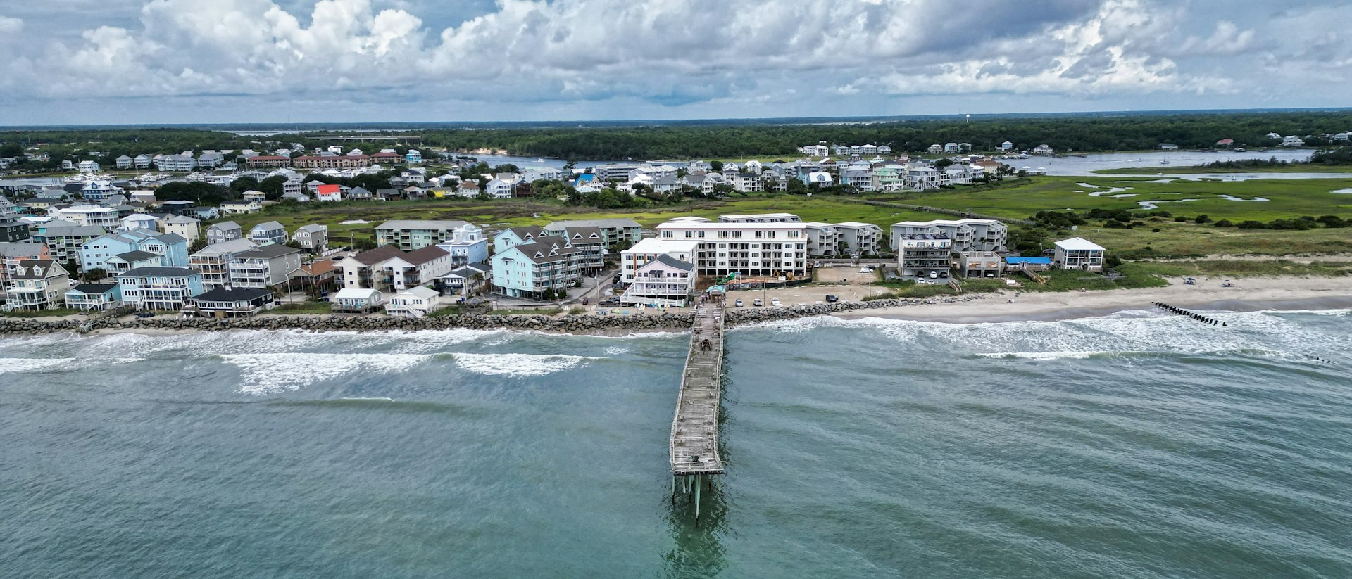 Aerial view of Carolina Beach, North Carolina, showing oceanfront homes, the fishing pier and the marsh behind the island.