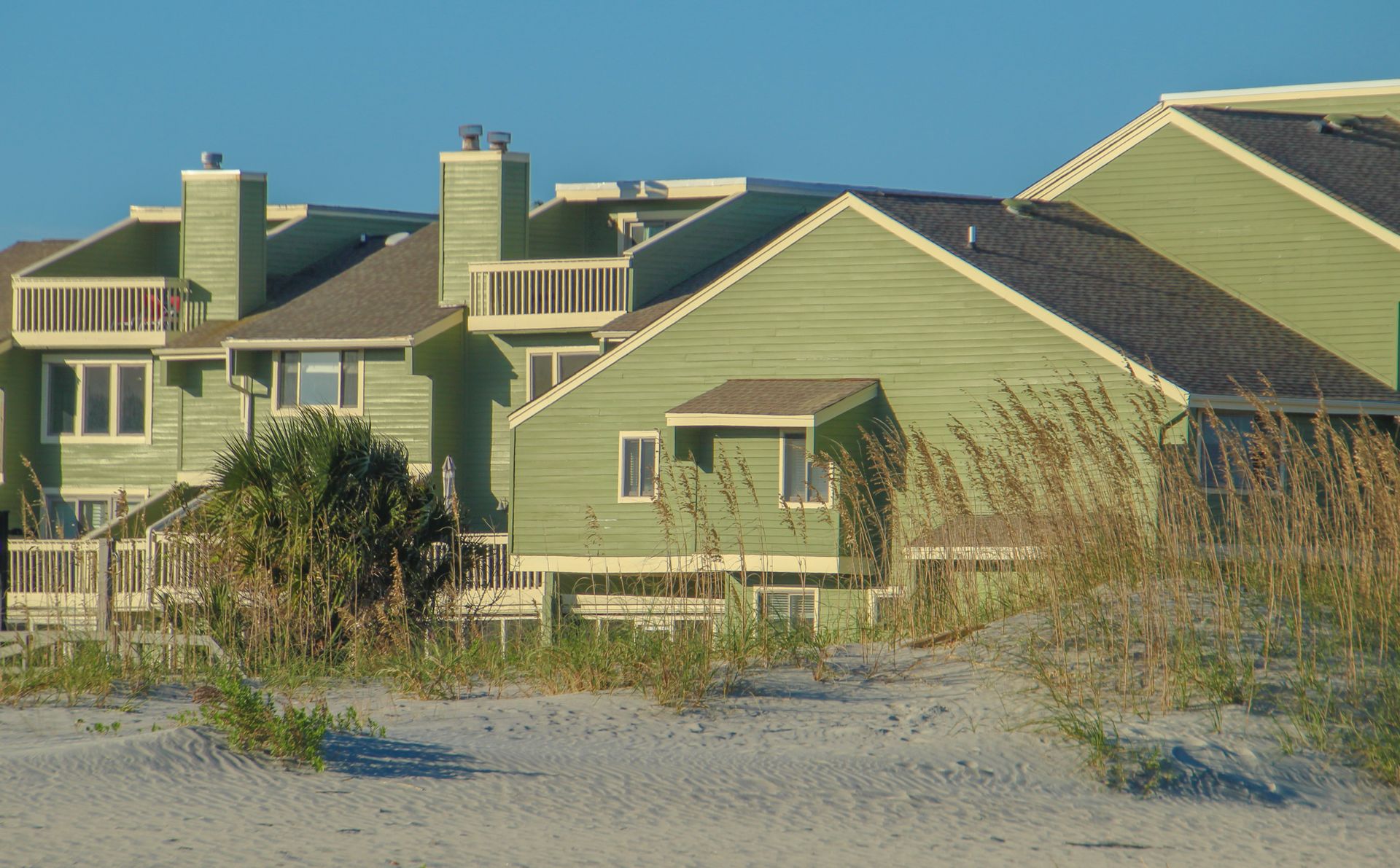 Green-sided oceanfront condominium buildings behind sea oats and sand