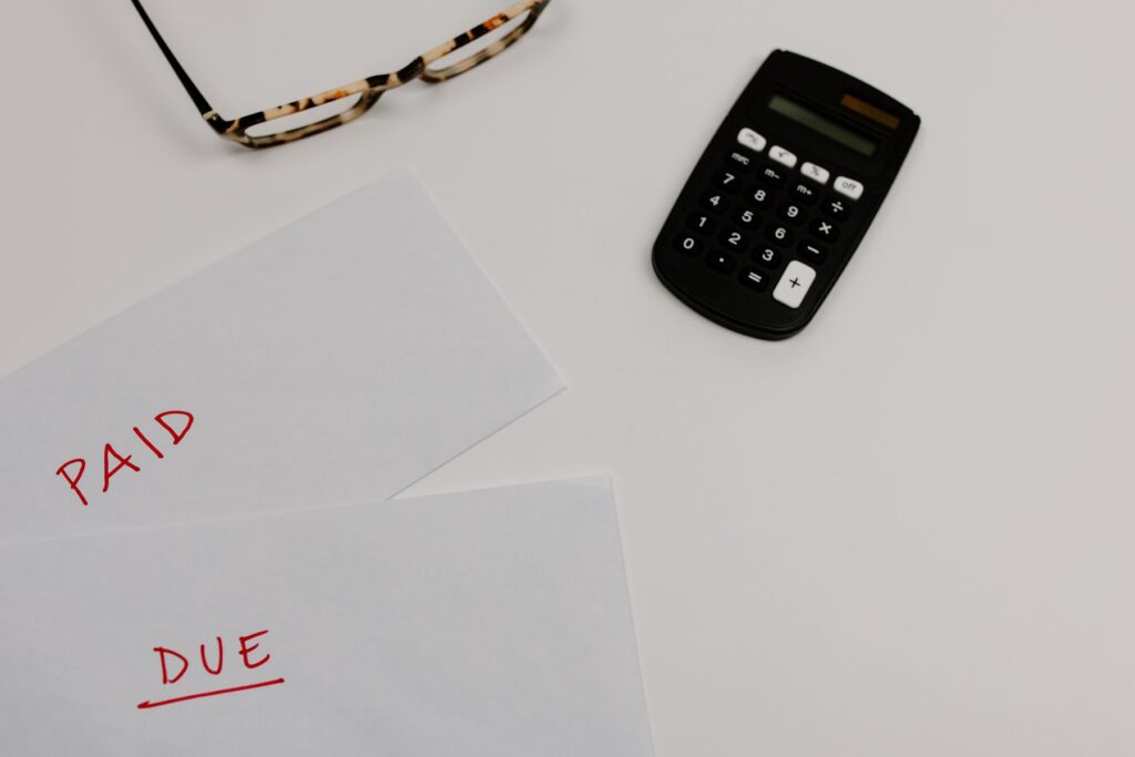 Household bills marked paid and due on a desk beside a calculator and reading glasses