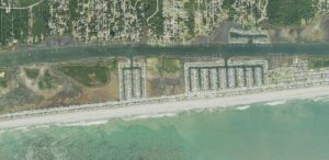 Aerial view of the center of Holden Beach, North Carolina, showing the oceanfront row of houses along the strand, the finger canals and private docks on the sound side, the Intracoastal Waterway behind the island and the mainland in Supply beyond it
