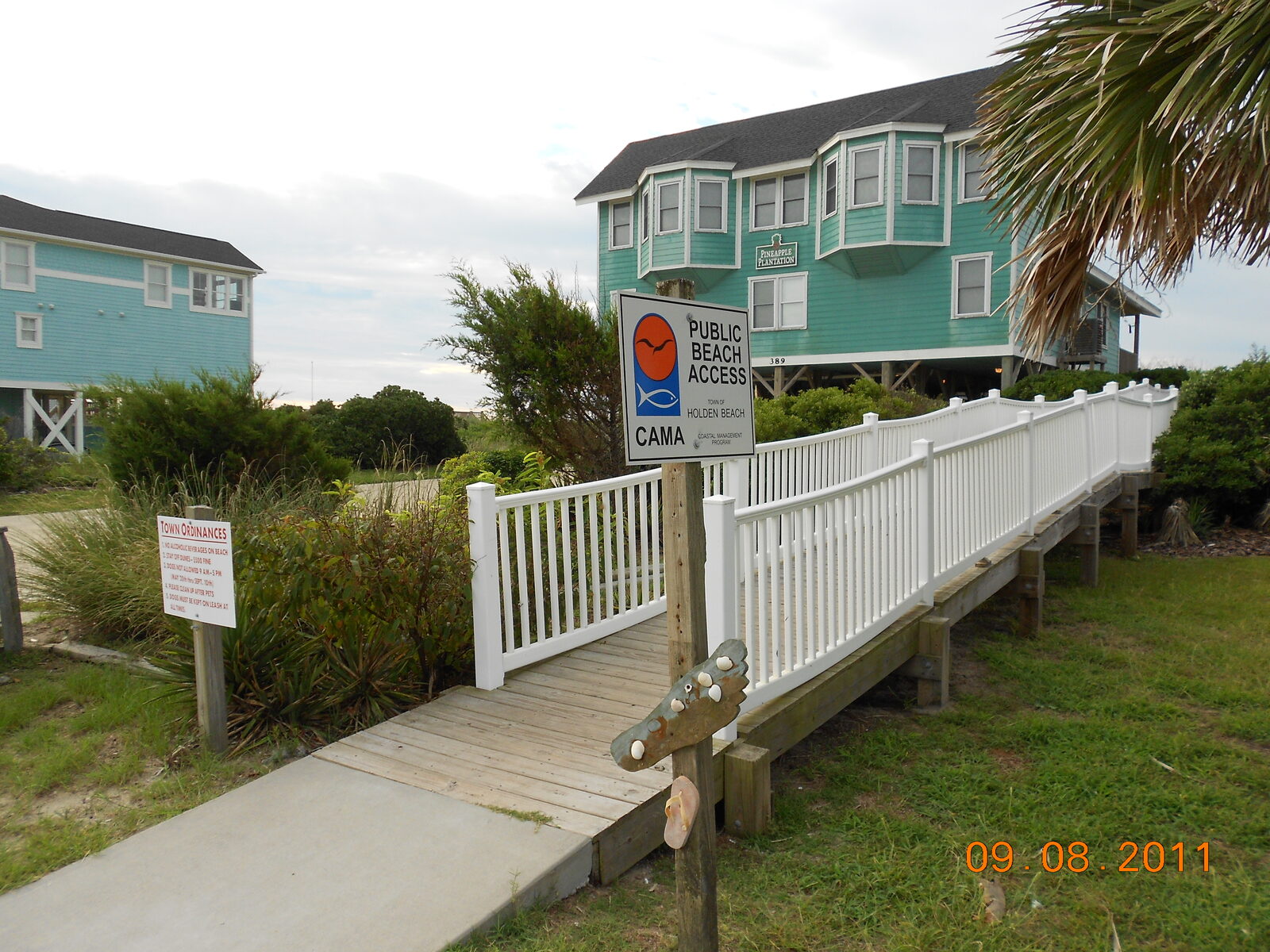 A Town of Holden Beach public beach access walkway with a CAMA public beach access sign and raised beach cottages behind it