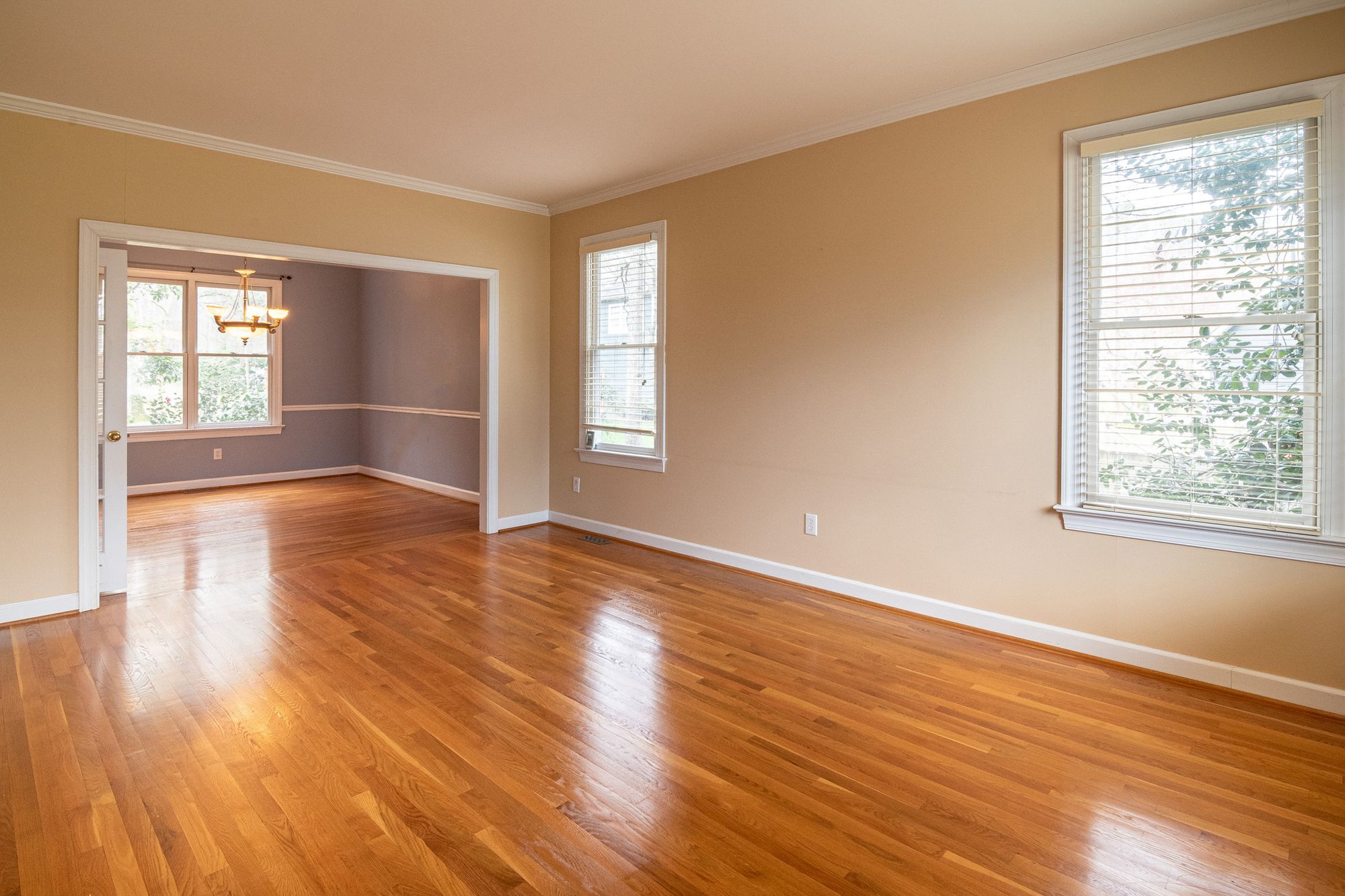 An empty living and dining room with hardwood floors and tan walls in an older single-family house, the condition most inherited homes are in when the family first sees them.