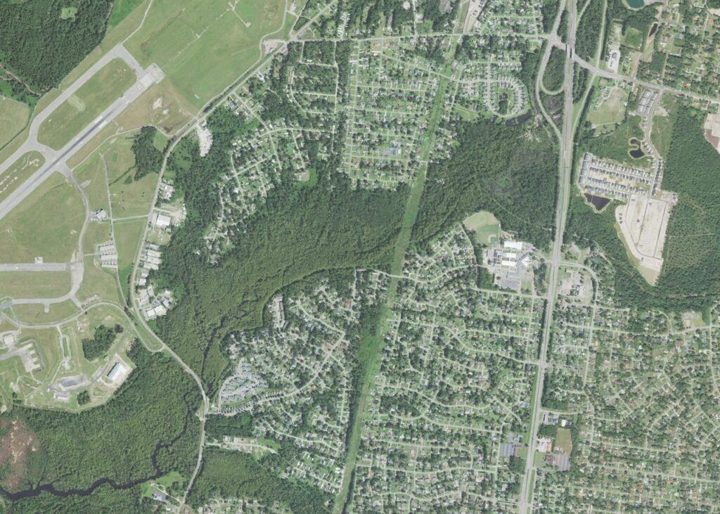 Aerial view of the western side of King's Grant in Wilmington, North Carolina, with the runways of Wilmington International Airport at left, wooded creek corridors through the center, and the Trask Middle and Laney High campuses on North College Road