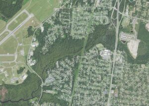 Aerial view of the western side of King's Grant in Wilmington, North Carolina, with the runways of Wilmington International Airport at left, wooded creek corridors through the center, and the Trask Middle and Laney High campuses on North College Road
