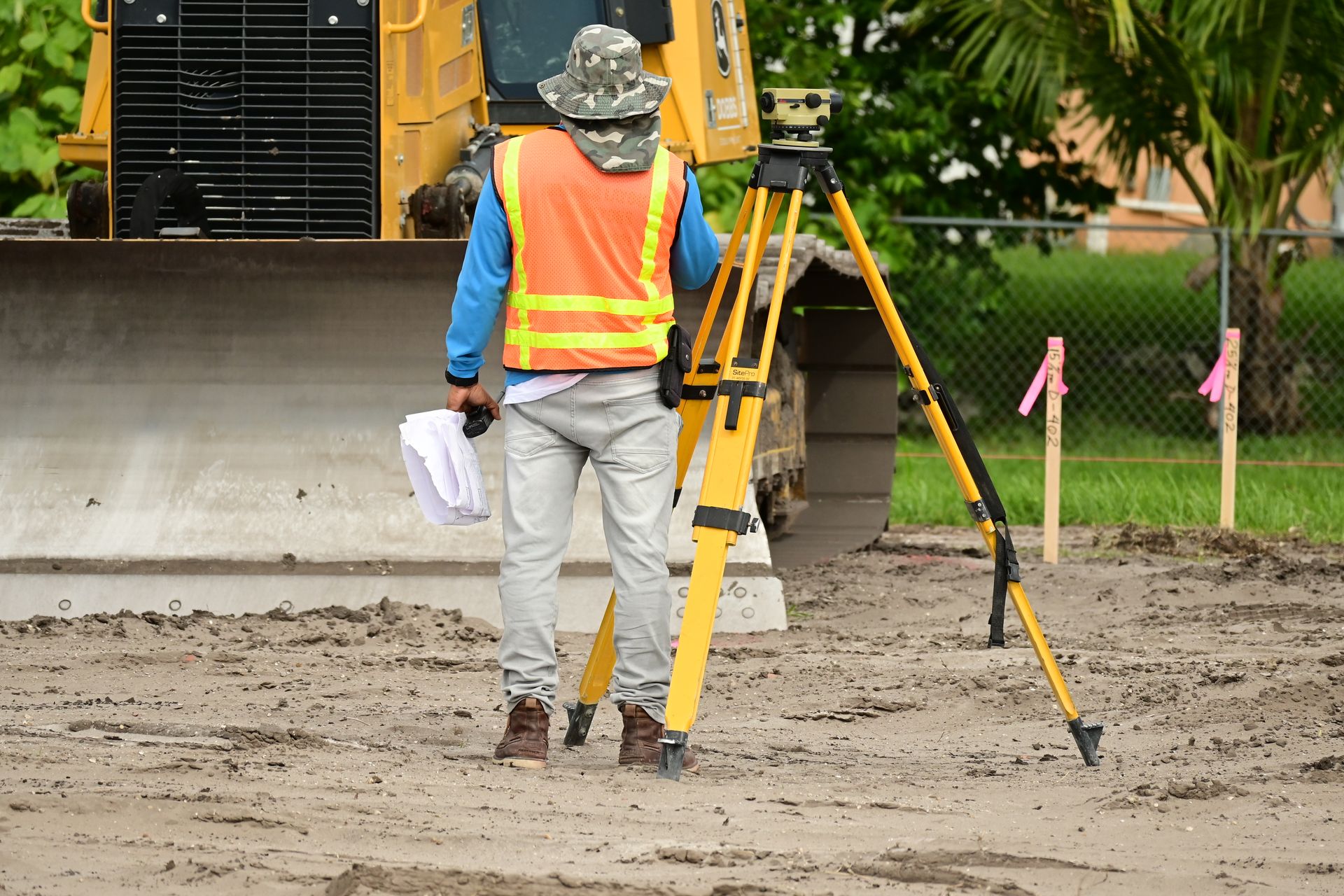 A land surveyor working with a tripod-mounted instrument beside flagged property stakes