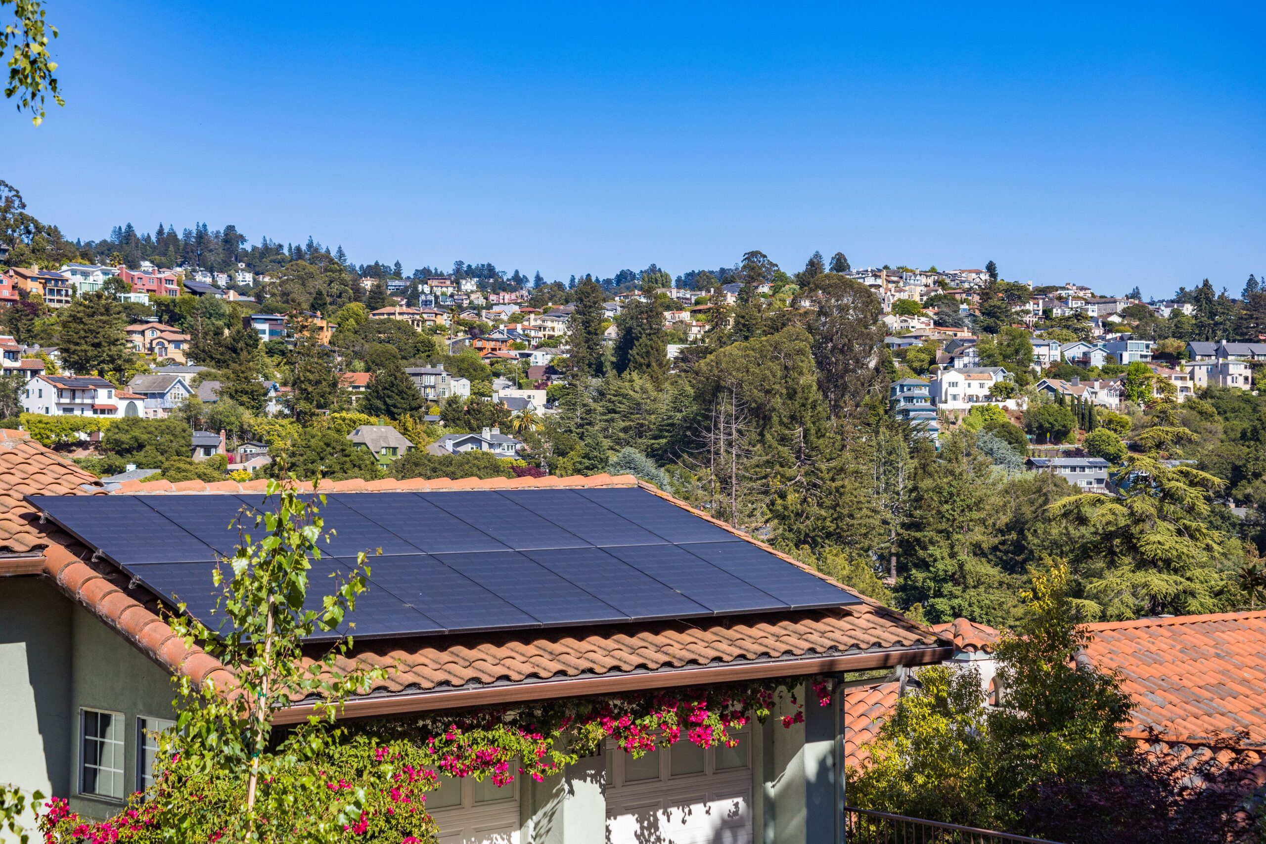 Solar panels mounted on the roof of a two-story suburban house under a clear sky