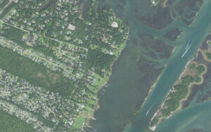 Aerial view of the sound side of Masonboro in New Hanover County, North Carolina, showing wooded neighborhoods off Masonboro Sound Road, private docks reaching across the marsh to the Intracoastal Waterway, and the undeveloped Masonboro Island Reserve beyond the channel