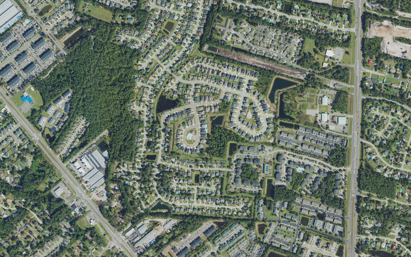 Aerial view of the residential area north of Monkey Junction in Wilmington, North Carolina, showing curving subdivision streets with stormwater ponds, long rows of townhomes and apartment buildings, and the Carolina Beach Road and South College Road corridors on either side