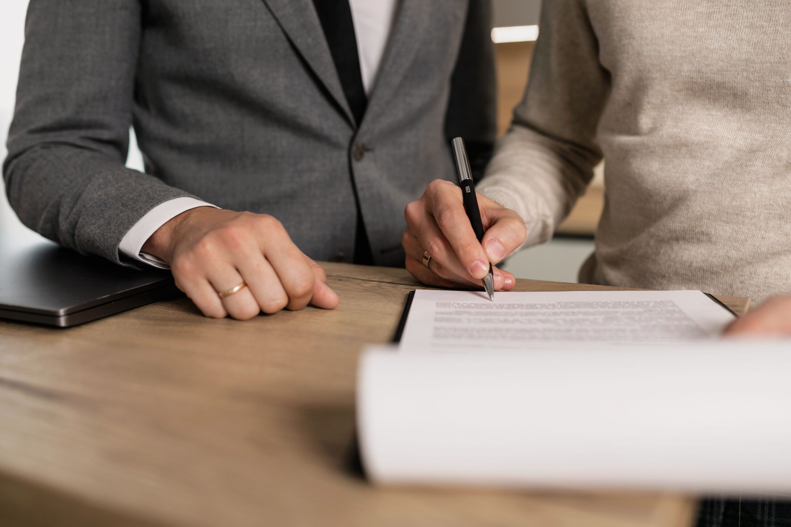 Two people signing closing documents at a wooden table in an office