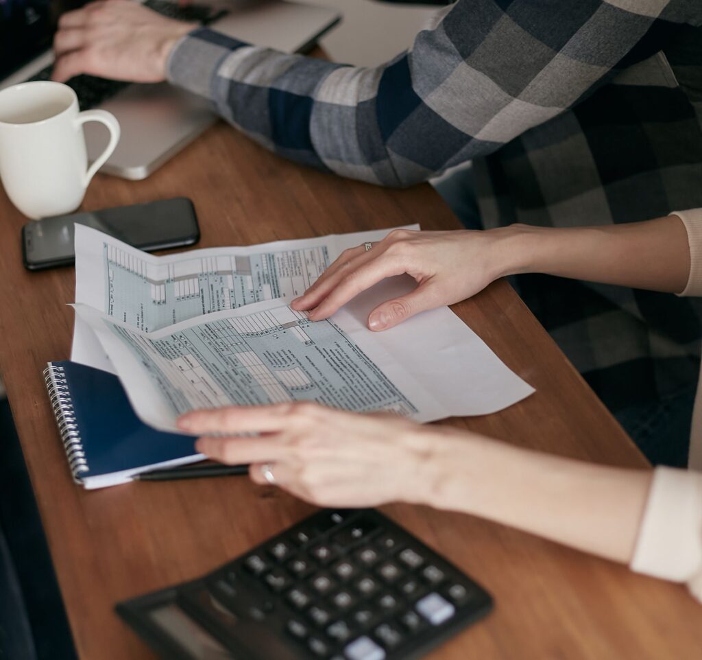 Two people reviewing printed tax forms at a table with a calculator and notebook