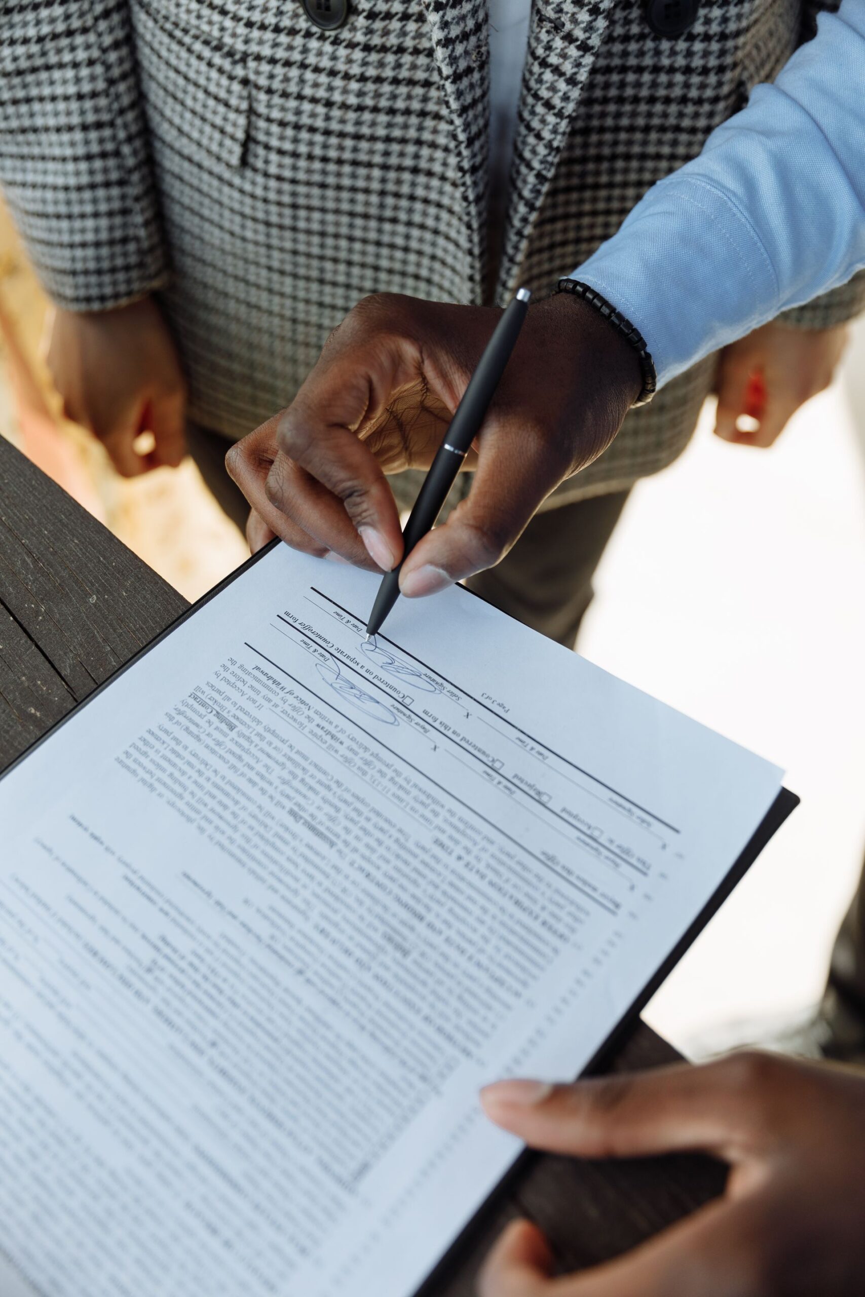 A person signing a real estate contract on a clipboard with a pen
