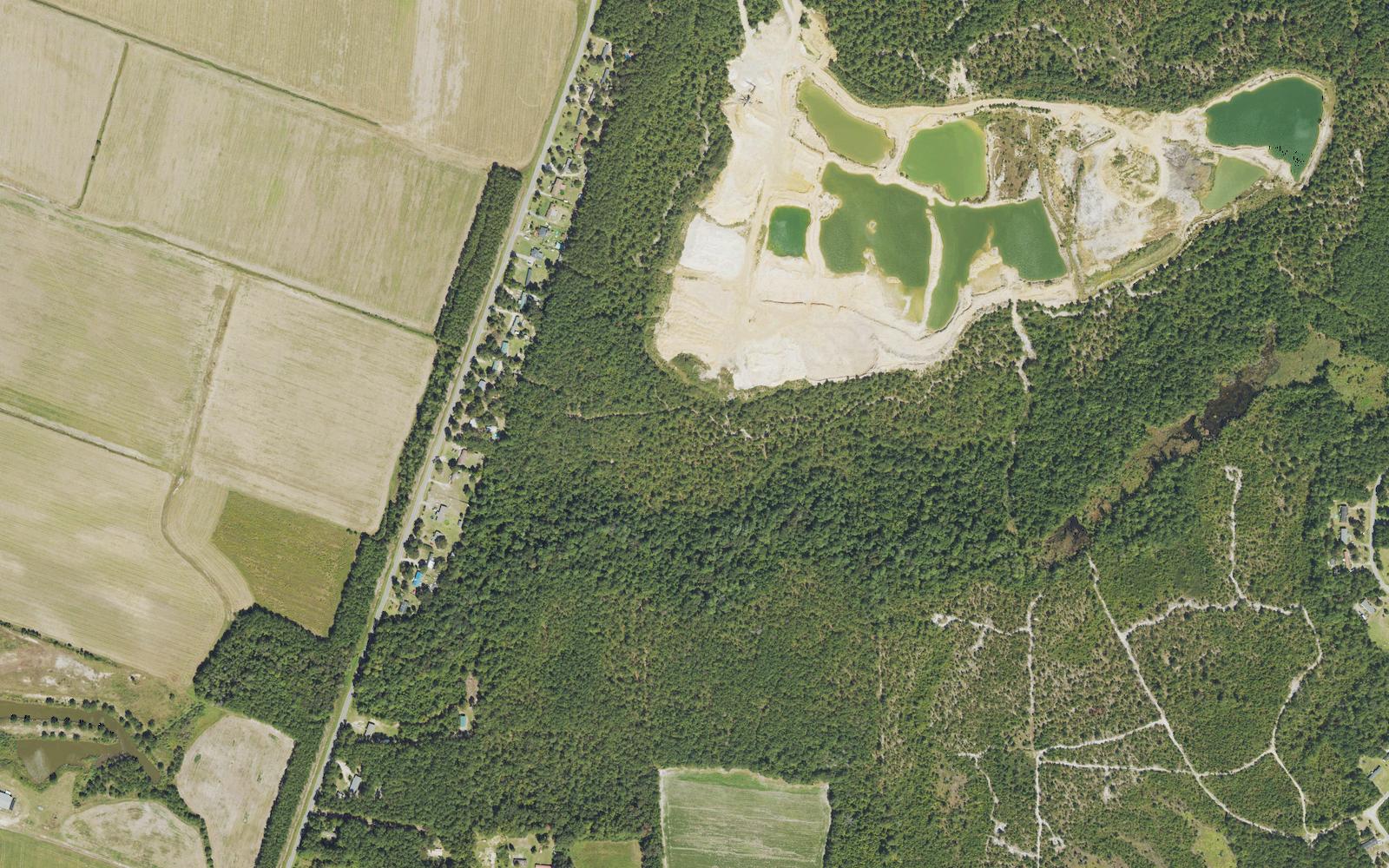 Aerial view of farm fields, roadside homes and a water-filled mine pit along Blue Banks Loop Road in Northwest, Brunswick County, North Carolina