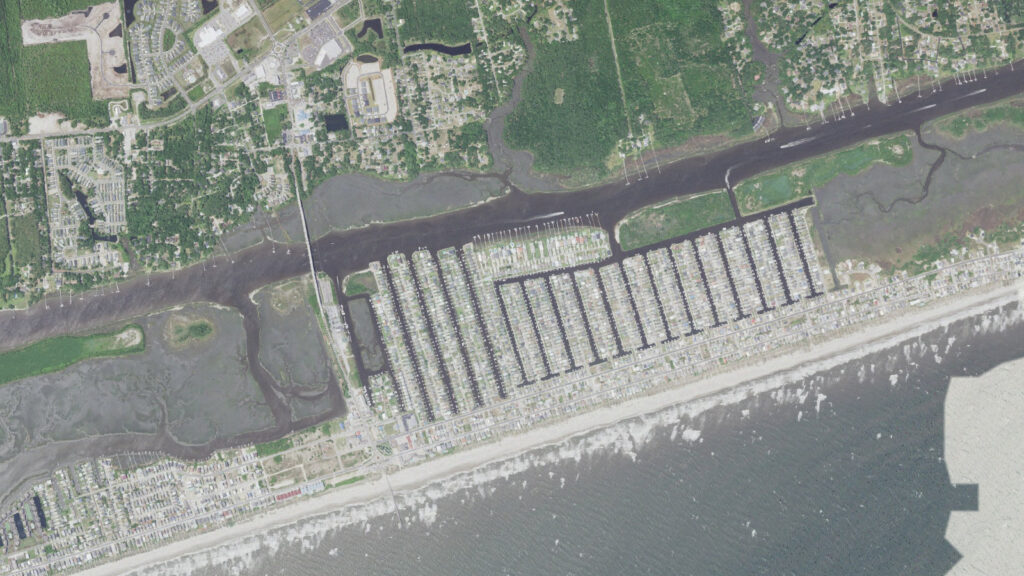 Aerial view of the center of Ocean Isle Beach, North Carolina, showing the Causeway Drive bridge crossing the Intracoastal Waterway from the mainland, the rows of finger canals and docks filling the sound side of the island, the beachfront street and the Atlantic surf along the strand