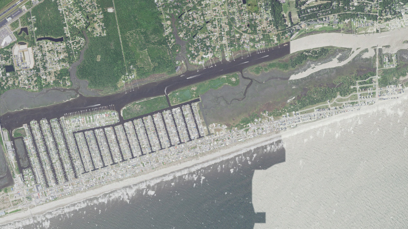 Aerial view of the east end of Ocean Isle Beach, North Carolina, with the finger canals and boat slips on the sound side, the beachfront row of houses along the strand, the Intracoastal Waterway running behind the island and the marsh and inlet shoals at the east end