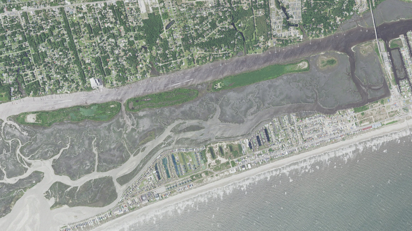 Aerial view of the west end of Ocean Isle Beach, North Carolina, showing the narrow western strand, the wide marsh and tidal flats between the island and the mainland, the Intracoastal Waterway channel and the Shallotte Inlet shoals beyond the west end