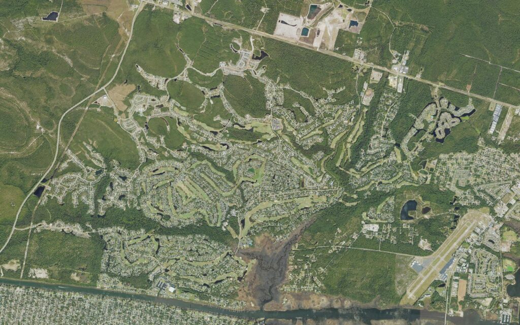 Aerial view of St. James Plantation in Brunswick County, North Carolina, showing four golf courses winding between residential streets and lagoons, N.C. 211 along the northern edge, the Intracoastal Waterway and Oak Island across the bottom, and the Cape Fear Regional Jetport at the right