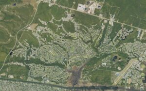 Aerial view of St. James Plantation in Brunswick County, North Carolina, showing four golf courses winding between residential streets and lagoons, N.C. 211 along the northern edge, the Intracoastal Waterway and Oak Island across the bottom, and the Cape Fear Regional Jetport at the right