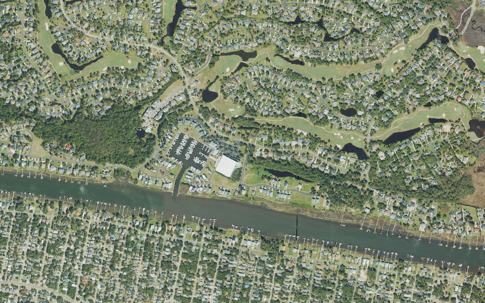 Aerial view of St. James Marina on the Intracoastal Waterway in Brunswick County, North Carolina, with its wet slips and dry stack storage building, golf fairways and homes behind it, and the streets of Oak Island across the water