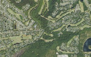 Aerial view of the eastern end of St. James Plantation, North Carolina, along St. James Drive, with golf holes, wooded lots, a large lake and residential streets