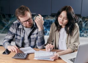 A couple at a kitchen table reviewing bills and a laptop with a calculator, working out what they can afford