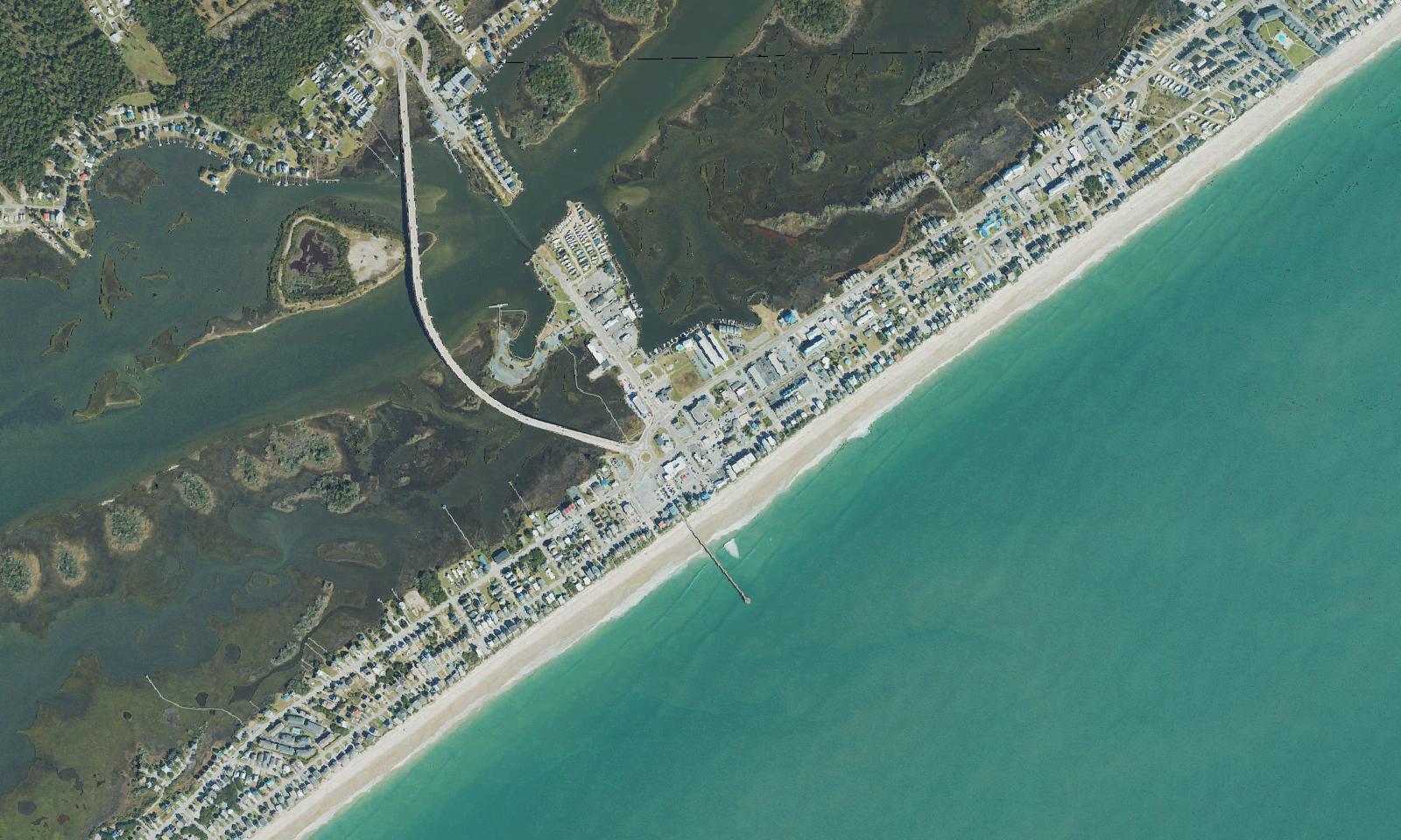 Aerial view of the center of Surf City, North Carolina, with the high-rise N.C. 50/210 bridge crossing the Intracoastal Waterway from the mainland, the roundabout and town center at the island end, the ocean pier reaching into the Atlantic and the marsh behind the island