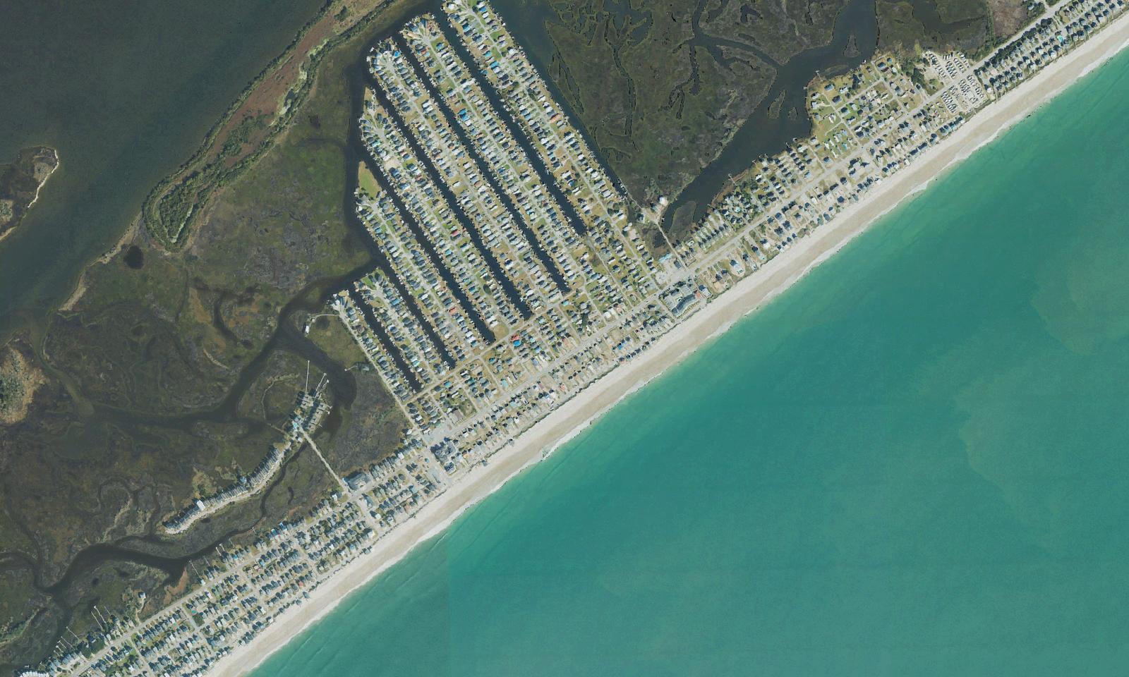 Aerial view of the north end of Surf City, North Carolina, showing the long rows of mobile and manufactured homes on the sound side, the beachfront streets along the strand, the marsh creeks behind the island and the Atlantic surf