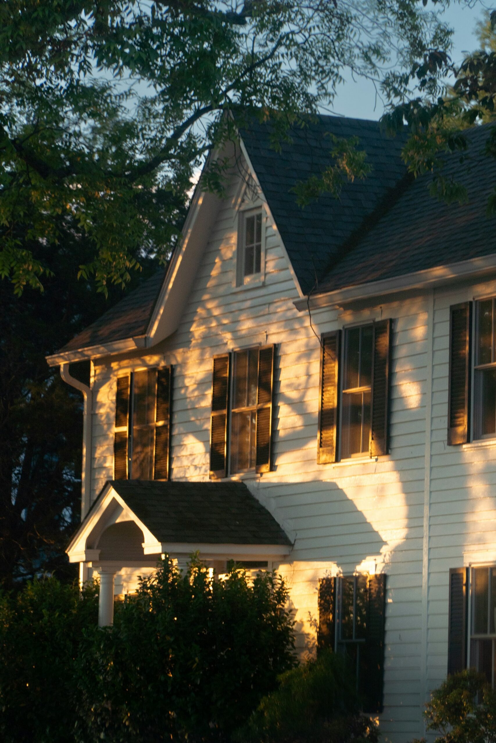 Classic white two-story home with dark shutters in warm golden-hour light