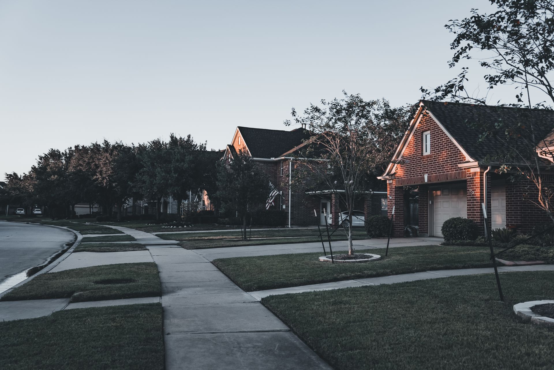 An established suburban street of brick homes with mature trees at dusk