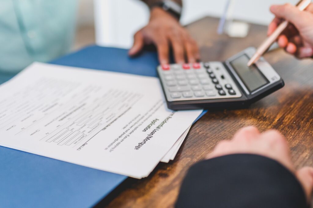 Hands using a calculator next to real estate documents on a desk
