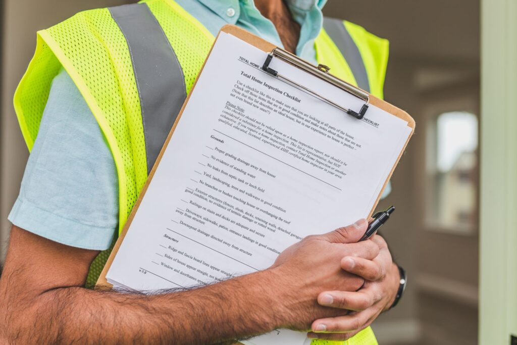 A home inspector in a safety vest holding a printed home inspection checklist on a clipboard