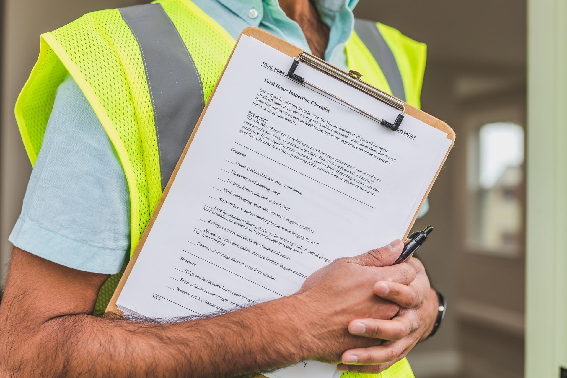 A home inspector in a safety vest holding a printed home inspection checklist on a clipboard