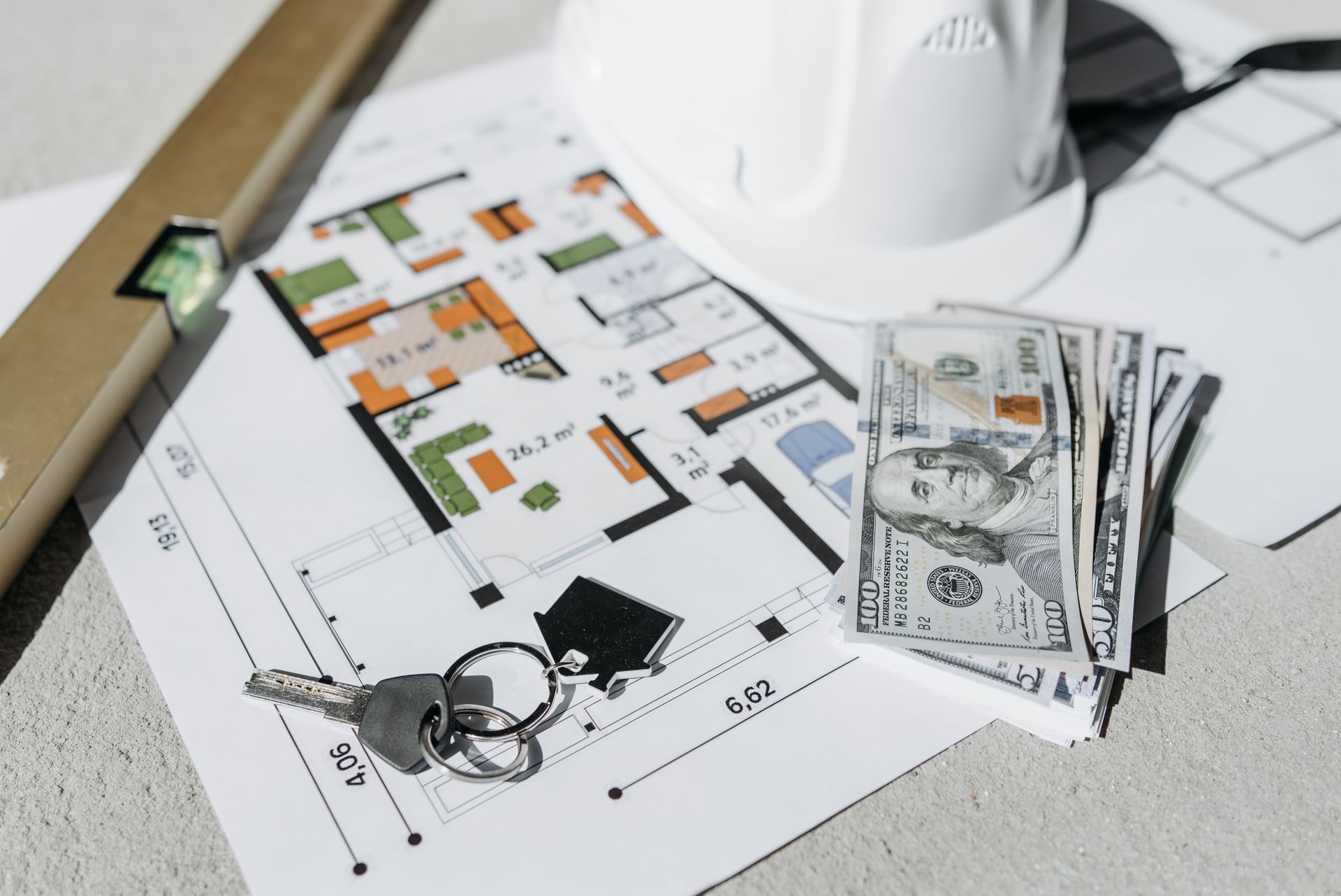 A floor plan on a table with cash, house keys and a hard hat, representing the money side of a home purchase